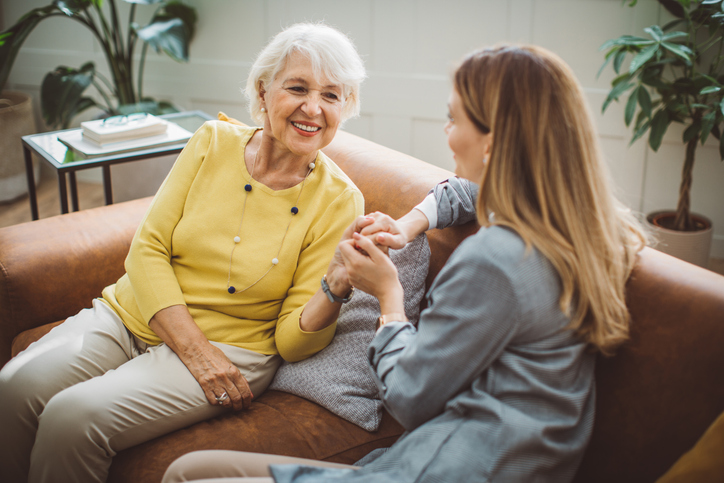 Older adult woman engages in conversation with adult daughter on couch.